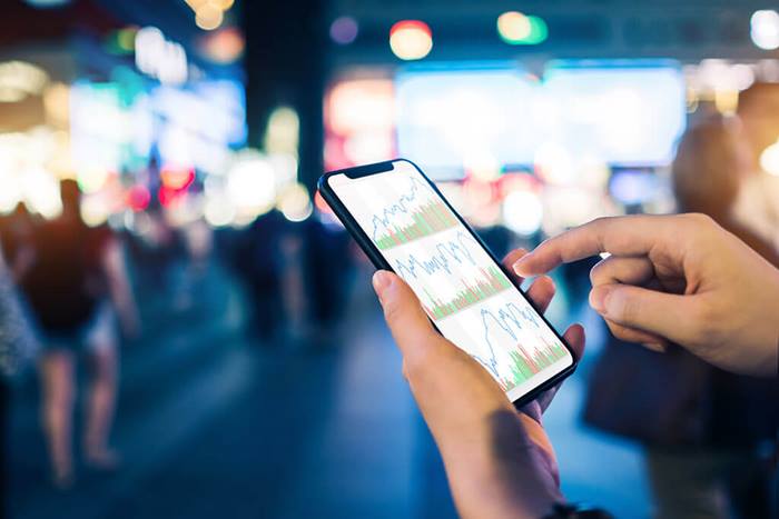 Close up of hands checking stock charts on smartphone in busy city street